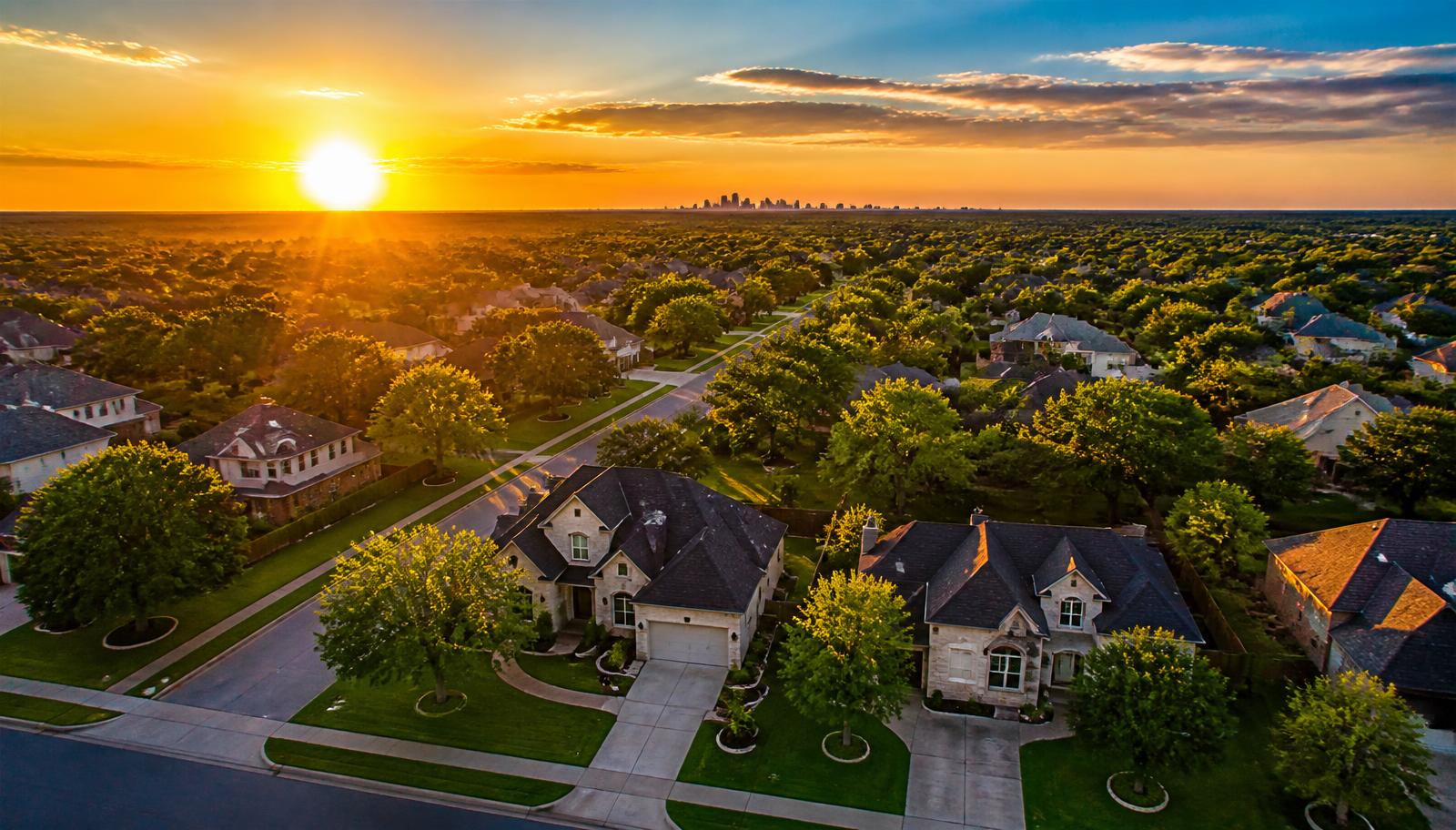 Aerial view of a suburban street glowing at golden hour with a skyline on the horizon
